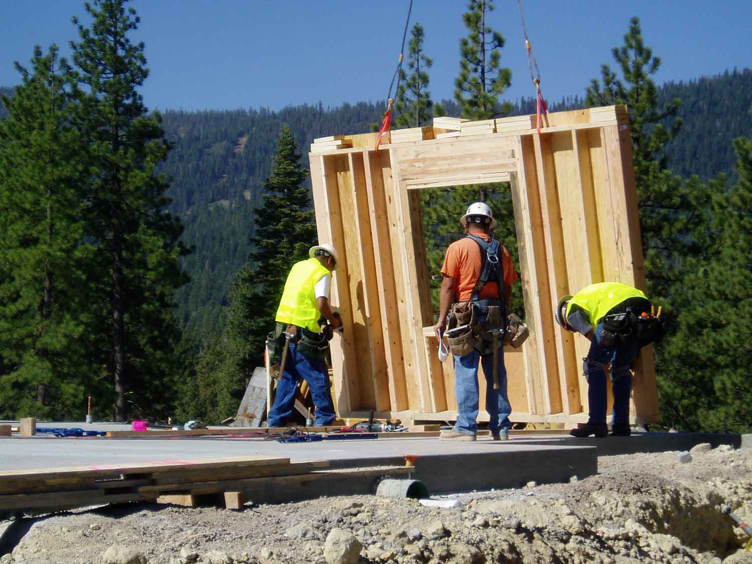 Three builders putting up a prefab wall on a concrete foundation